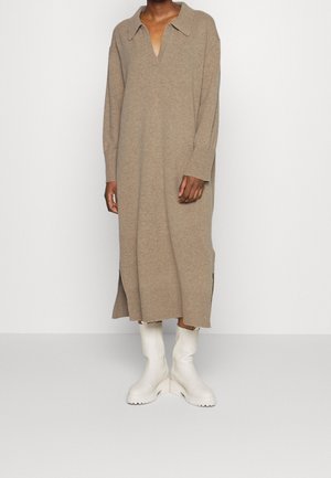 Robe en tricot beige avec un col, des manches longues, des fentes latérales, associée à des bottines blanches. Texture douce et coupe ample.