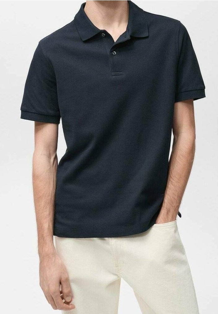 Polo bleu marine en coton lisse avec un col classique, trois boutons et des manches courtes. Porté avec un pantalon de couleur claire.