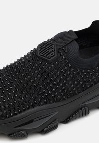 Black sneaker with textured upper featuring small sparkling details. Slip-on design with a logo accent and a sturdy rubber sole.