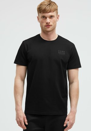 Schwarzes Baumwoll-T-Shirt mit kurzen Ärmeln, Rundhalsausschnitt und subtiler "CAMP DAVID SPORT"-Logoprint auf der Brust. Glatte Textur.