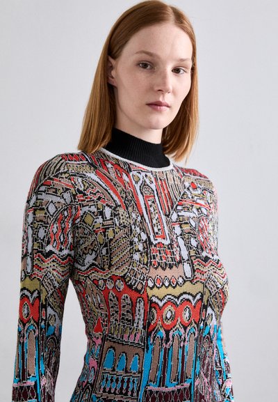 Pull en maille avec un col haut noir, présentant un motif géométrique coloré en rouge, bleu, jaune et noir, en tissu texturé.
