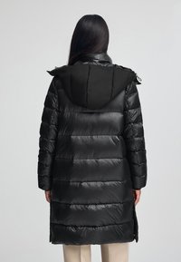 Czarna kurtka puchowa z kapturem, z poziomym pikowaniem, błyszczącą teksturą i bocznymi zamkami. Długość sięga do połowy ud.