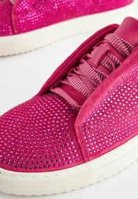 Zapatilla rosa con una superficie texturizada adornada con brillantes rhinestones. Presenta una lengua acolchada y cordones planos, con una suela de goma blanca.
