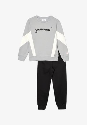 Felpa grigia con strisce diagonali bianche e scritta "CHAMPION" abbinata a pantaloni jogger neri.