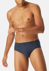 Caleçons de bain bleu marine avec des rayures verticales blanches, fabriqués en tissu extensible. Présente un design ajusté et une ceinture lisse.
