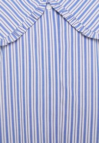 Blå och vit randig skjorta med krage och volangkant, har knäppning med knappar och vertikala ränder i varierande bredd.