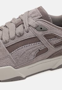 Szare zamszowe sneakersy z teksturowanymi akcentami, grubymi sznurowadłami i gumową podeszwą. Posiadają kanciaste wycięcia i subtelne logo po bokach.