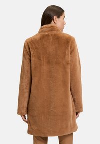 Brun faux fur frakke med en blød, tekstureret overflade, lange ærmer og krave; strækker sig forbi hofterne. Fås i en afslappet stil.