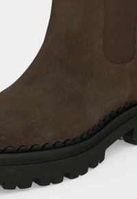 Bottine en daim marron avec panneau latéral élastique et semelle épaisse en caoutchouc noir crantée pour une bonne adhérence et durabilité.