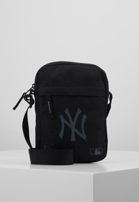 Borsa a tracolla nera in tela con logo NY grigio, apertura superiore con zip, tracolla regolabile e taschino frontale. Forma piatta e quadrata.