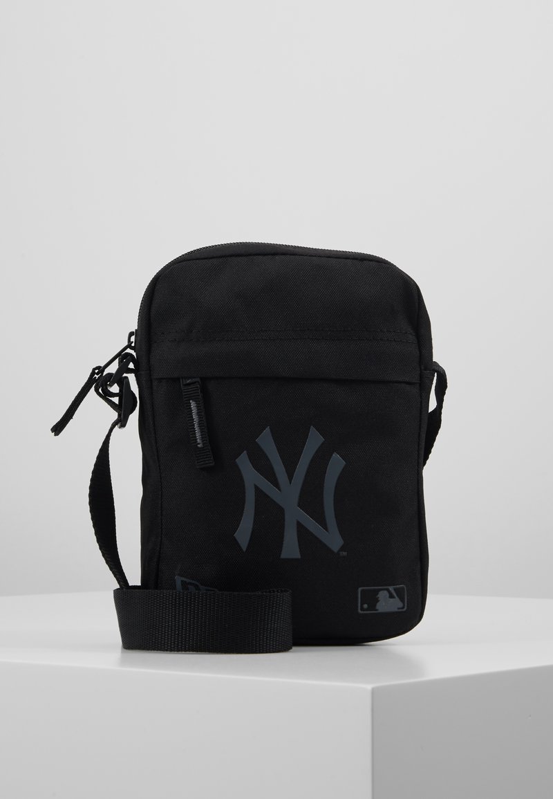 Borsa a tracolla nera in tela con logo NY grigio, apertura superiore con zip, tracolla regolabile e taschino frontale. Forma piatta e quadrata.