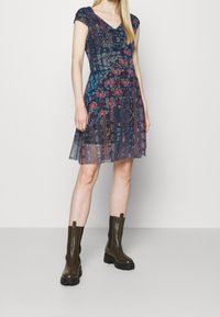 Blomstertryckt klänning med V-ringning, korta ärmar och lagerdesign. Färger inkluderar blått, rött och kräm. Bärs med bruna knä-höga stövlar.