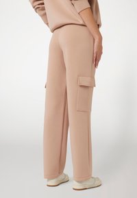 Šviesiai rožinės, aukštu liemeniu sportinės kelnės su tiesiu kirpimu. Yra dvi didelės šoninės kišenės ir glotnus paviršius.