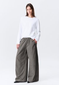 Pantalon à jambes larges en tissu de coton vert olive avec une taille élastique. Associé à un haut blanc à manches longues. Texture lisse, design minimaliste.