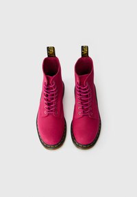 Bottines en cuir rose à bout rond, avec des semelles noires contrastées et des coutures jaunes. Elles disposent de huit œillets et d'un système de laçage.
