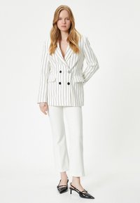 Blazer cruzado en blanco con rayas verticales negras, combinado con pantalones blancos y tacones slingback de charol negros. Incluye bolsillos laterales.