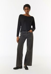 Schwarzer Pullover mit Boot-Ausschnitt, kombiniert mit hoch taillierten, weit geschnittenen grauen Jeans und schwarzen Slippern. Schlichtes Design mit entspannter Passform.