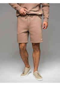 Shorts in pile beige con vita regolabile, tasche laterali e una piccola etichetta del marchio. Abbinati a sneaker beige basse. Texture liscia.