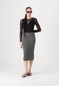 Haut noir à manches longues en matière transparente, associé à une jupe crayon noire et blanche à motifs, et des sandales noires à lanières. Lunettes de soleil incluses.