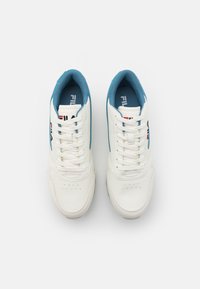 Vita sneakers med blå accenter, slädt läderöverdel, rund tå, perforerade detaljer och platta vita snören. Varumärkeslogotyp på sidan.