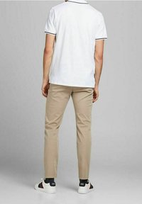 Maglietta polo bianca con dettagli del colletto neri, abbinata a pantaloni beige e sneakers bianche con strisce nere e rosse.