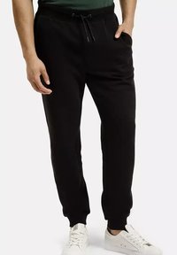 Czarne dresowe spodnie z regulowanym pasem na sznurku, bocznymi kieszeniami, ściągaczami u dołu i gładką fakturą. Nosi się je z białymi trampkami.