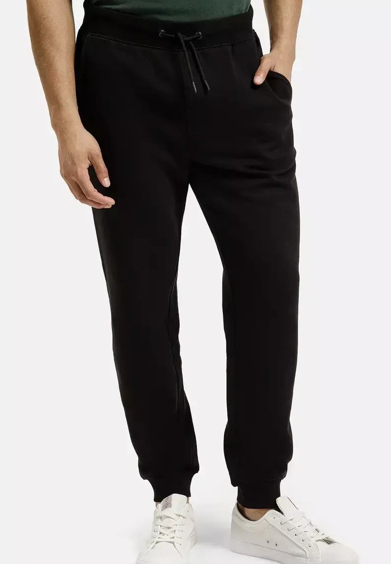 Czarne dresowe spodnie z regulowanym pasem na sznurku, bocznymi kieszeniami, ściągaczami u dołu i gładką fakturą. Nosi się je z białymi trampkami.
