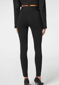 Leggings neri con vita alta e design aderente. Il materiale è liscio con una consistenza senza cuciture. Indossati con tacchi neri.