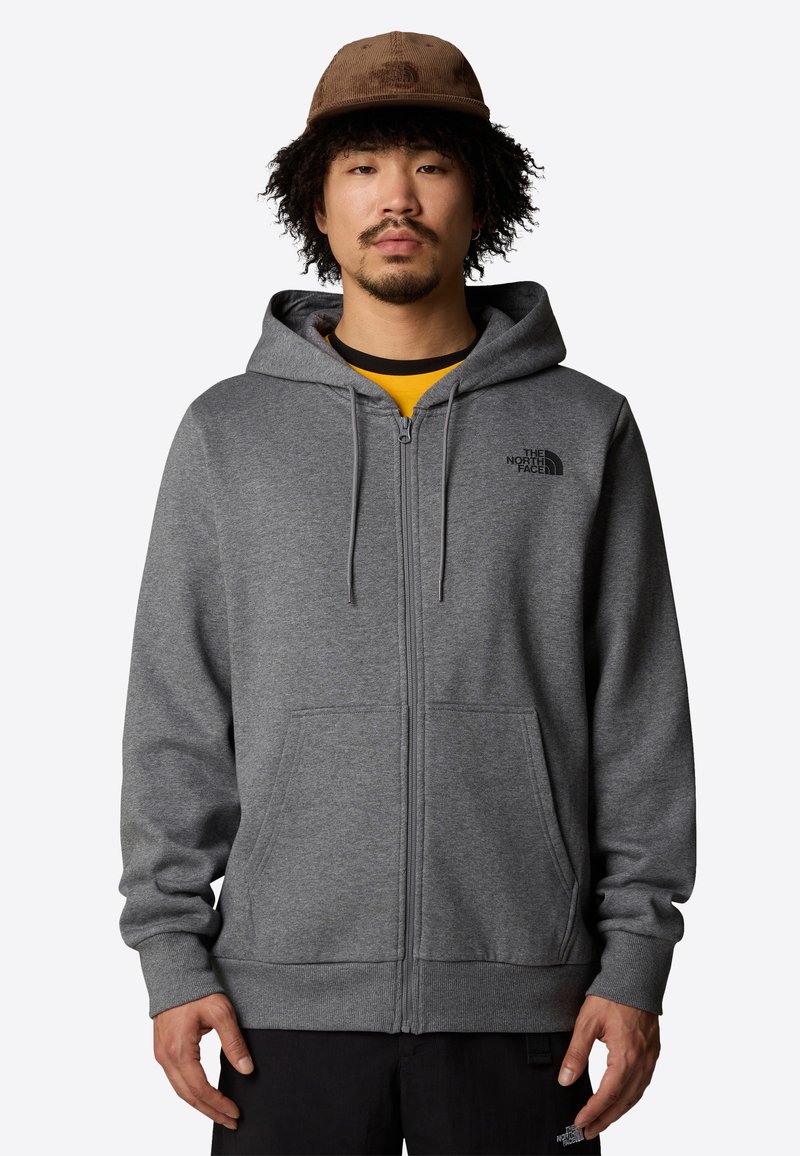 Sudadera gris con cremallera y bolsillo canguro, que cuenta con una capucha ajustable y un logo negro en el pecho. La tela parece suave con una textura lisa.