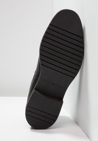 Musta nahkakengän pohja, jossa on vaakasuorat urat pidon parantamiseksi. Kenkä on pyöristetty muotoiltu ja hieman kapeneva kärkeen päin. Koko 41 merkattuna.