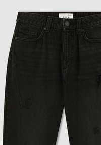 Czarne dżinsy charakteryzują się wysokim stanem, przetarciami oraz tradycyjnym pięciopakowym designem z zapięciem na guzik z przodu.