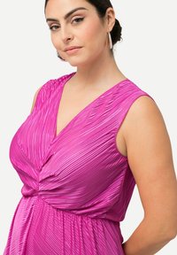 Fuchsiové plisované šaty s hlubokým výstřihem do V, bez rukávů a shromážděným detailem v pase. Hladká, lesklá látka s vertikálními sklady.