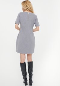 Grijze jurk met korte mouwen en een rits aan de achterkant, tot op de knie met een getailleerde silhoeet, gecombineerd met zwarte kniehoog laarzen.