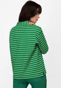 Maglia a maniche lunghe a righe verdi e bianche con colletto alto, caratterizzata da un fit rilassato e fessure laterali. Tessuto a costine, design casual.