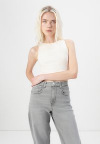 Lichtbeige geribde tanktop gecombineerd met grijze hoge taille jeans. De stof lijkt zacht, met een nauwsluitend ontwerp en minimale stikdetails.