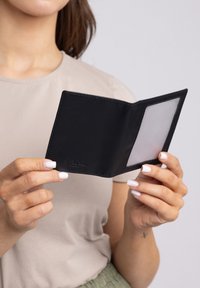 Zwarte leren portemonnee met een gevouwen ontwerp, met een doorzichtige insteek aan de ene kant en geperst merklogo. Strakke textuur en minimalistische afwerking.