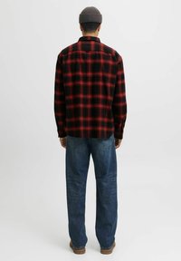 Röd och svart rutigt flanellskjorta med långa ärmar, avslappnad passform, som bärs med blå denimjeans. Bakåtsidan visar en knappkrage och textil med struktur.