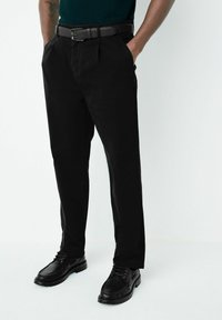 Sorte bukser lavet af bomuld med en tekstureret overflade, der har sidelommer og lige snit, kombineret med sorte snørebåndssko.