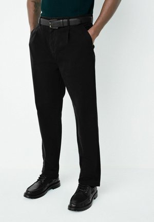 Black trousers made of cotton with a textured surface, featuring side pockets and a straight cut, paired with black lace-up shoes.