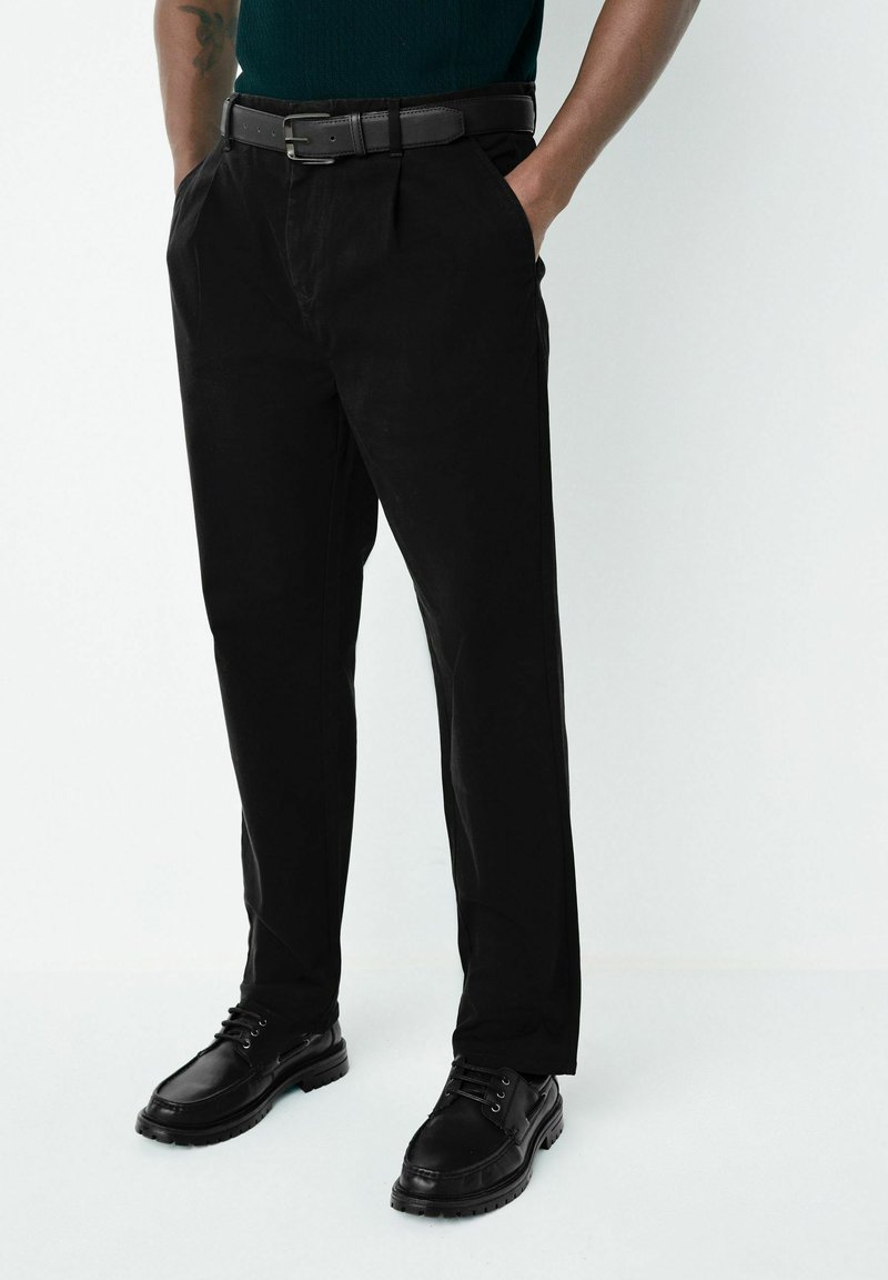 Sorte bukser lavet af bomuld med en tekstureret overflade, der har sidelommer og lige snit, kombineret med sorte snørebåndssko.