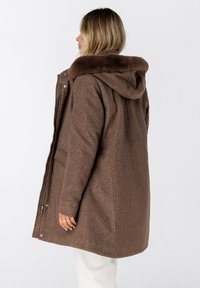 Bruine wollen blend jas met een afneembare capuchon. Voorzien van een rits aan de voorkant, zijzakken en een zacht, gestructureerd kraagje.