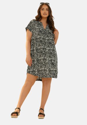 Robe à motifs noir et blanc avec des manches courtes, un décolleté en V et une coupe décontractée. Portée avec des sandales noires à brides et une coiffure lisse.