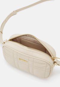 Béžová prošívaná kabelka přes rameno se zipem na vrchu, zlatými kovovými doplňky a nastavitelným popruhem. Vnitřek má hladkou podšívku a karty na vložení karet.