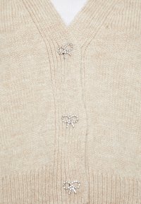 Beige knitted cardigan featuring a V-neck, three decorative bow-shaped buttons embellished with rhinestones. Soft texture with ribbed edges.