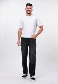 Balti medvilninė marškinėliai derinami su juodomis džinsinėmis kelnėmis, pasižyminčiomis siūlių detalėmis, dėvimi su juodai baltais sportbačiais. Paprastas, kasdienis stilius.