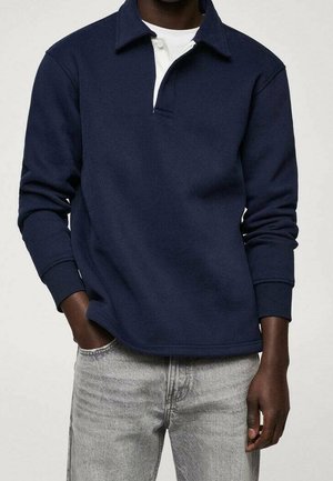 Marineblå sweatshirt med lange ærmer og krave, der har en hvid undertrøje, der stikker ud ved halsudskæringen, lavet af et blødt materiale.