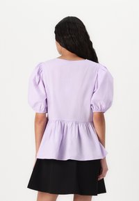 Lilla peplum topp med pufferm, laget av lett stoff, har en samlet midje og enkel rund hals.
