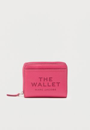 Vaaleanpunainen, teksturoitu nahkainen vetoketjellinen lompakko, jossa etupuolella kohopainatus "THE WALLET MARC JACOBS" ja pieni ranneke.