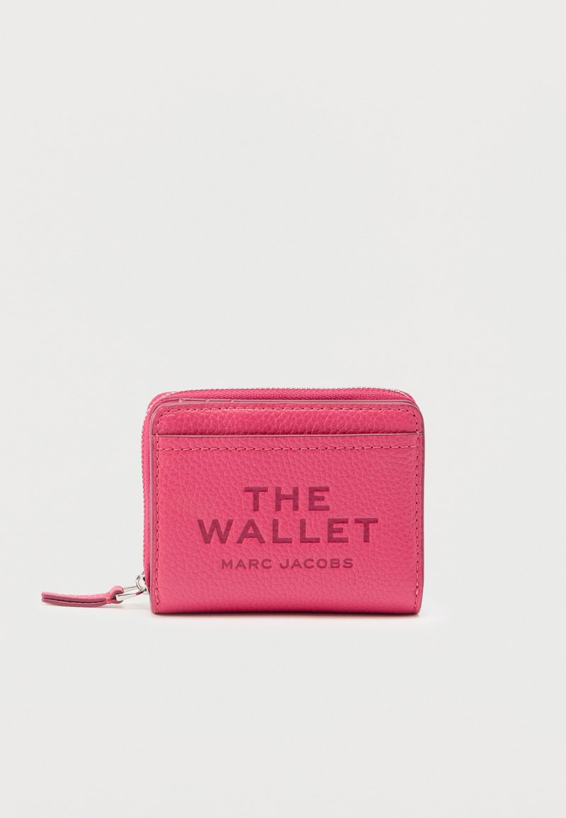 Portefeuille rose en cuir texturé avec fermeture à glissière autour, embossé de "THE WALLET MARC JACOBS" sur le devant et une petite bride de poignet.