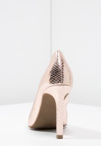 Scarpa con tacco alto in oro rosa con una texture a tema serpente, punta affilata e tacco sottile. Il materiale è lucido e liscio.